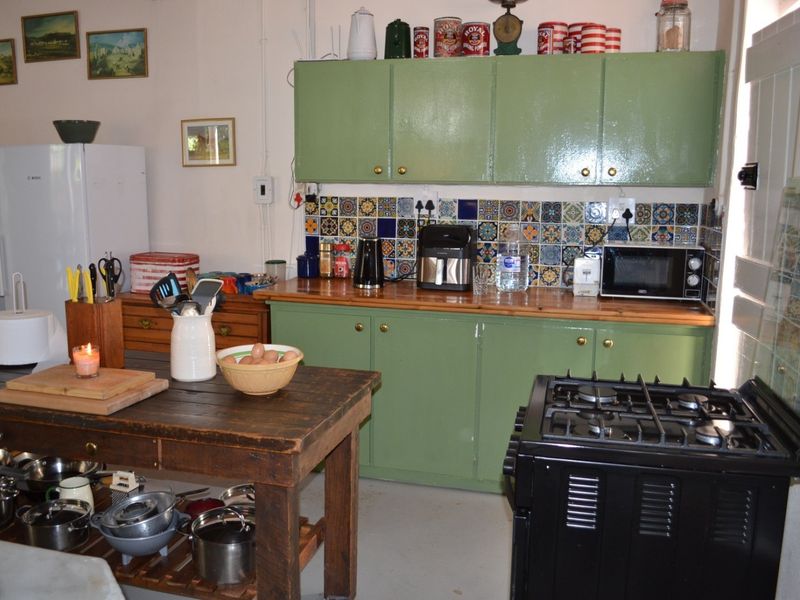 A rustic kitchen featuring green painted cabinetry, a wooden countertop, and a decorative patterned tile backsplash with a freestanding gas stove.