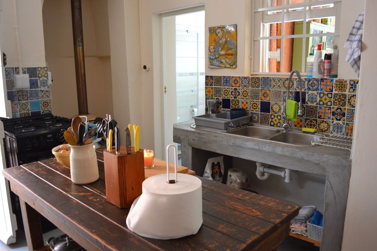 A rustic kitchen featuring a concrete countertop with a double sink, decorative tiled splashback, and a freestanding gas stove with a wood-burning fireplace.