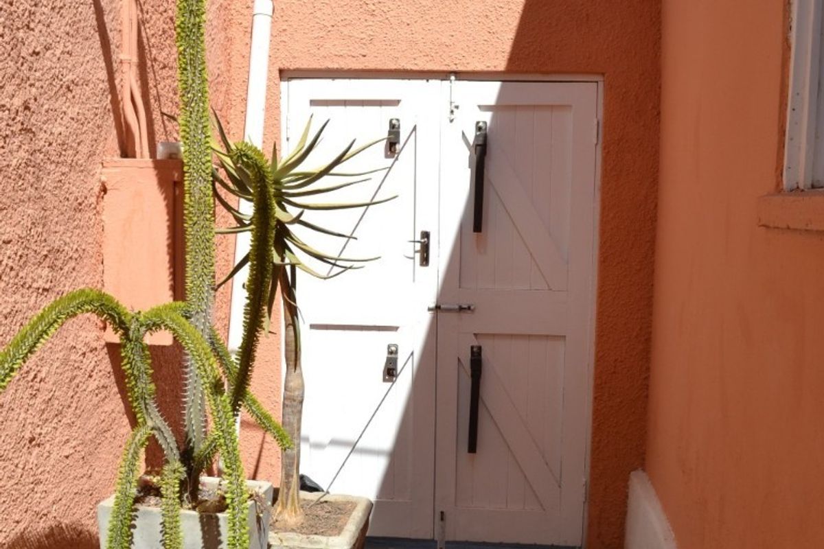 A narrow rear exterior passage featuring textured peach-colored walls, concrete flooring, and a white double door entrance.