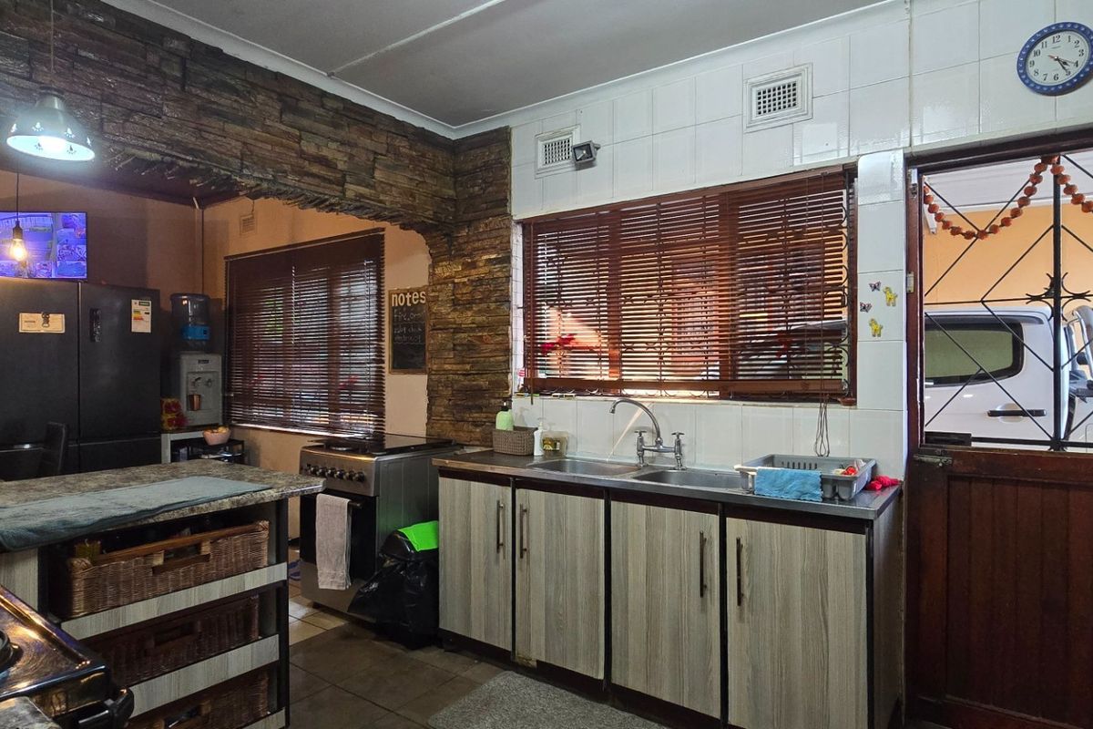 A functional kitchen featuring stone veneer accents, laminate cabinetry, a double sink, and a freestanding stove with direct access to the exterior.