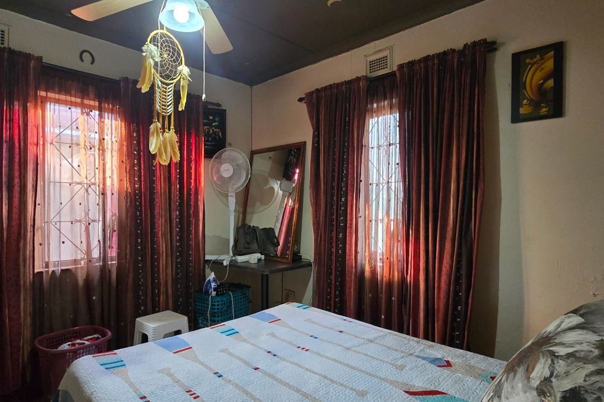 A bedroom featuring dual windows with security bars, a ceiling fan, and visible wall surface wear requiring maintenance.