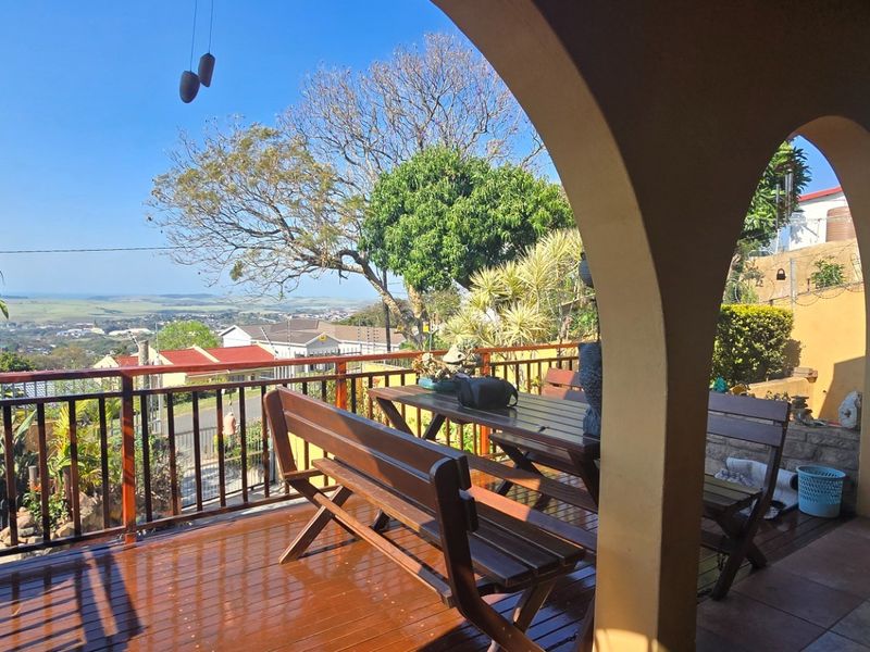Covered patio featuring arched masonry columns, timber decking, and a timber balustrade, offering elevated views of the surrounding landscape.