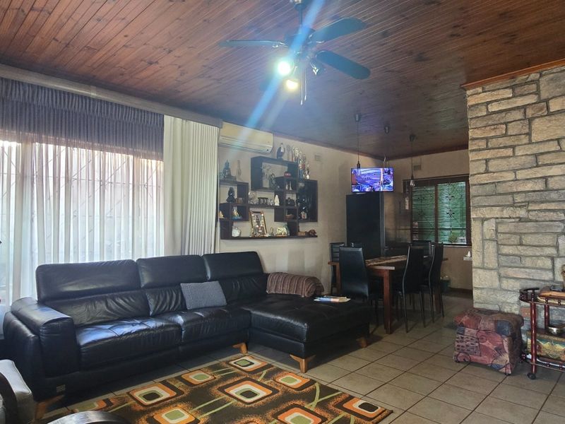 Open-plan living and dining area featuring a distinctive stone feature wall, timber-clad ceiling, tiled flooring, and a ceiling fan.
