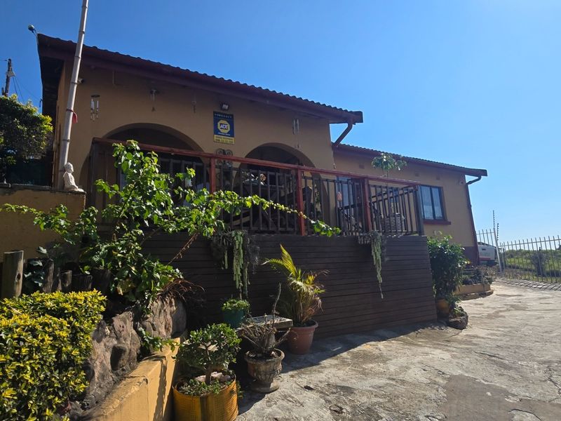 Front elevation of the house featuring a raised timber deck, concrete driveway, and secure perimeter fencing.