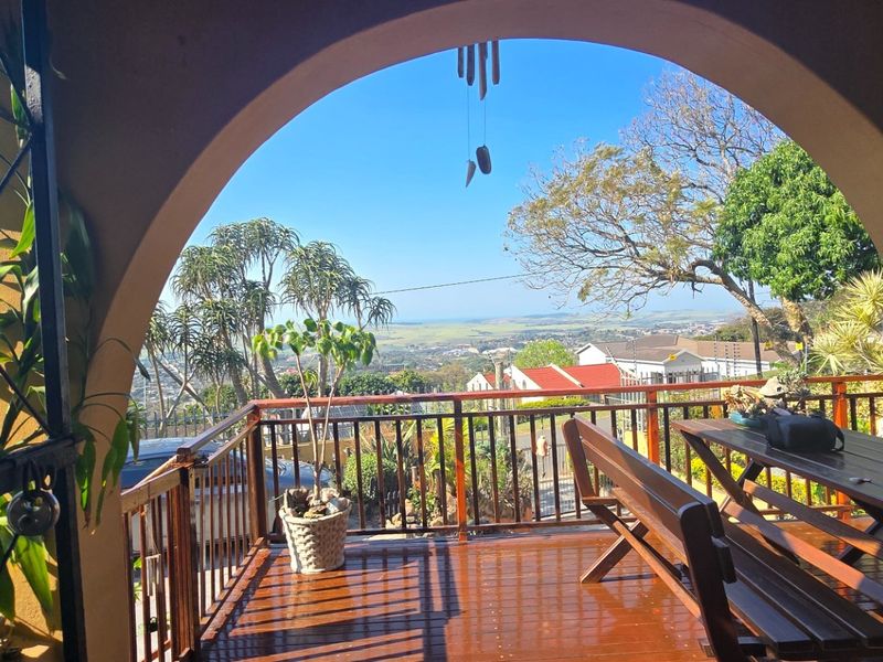 Covered patio featuring wooden decking, a metal balustrade, and an arched opening framing expansive elevated views of the surrounding landscape.