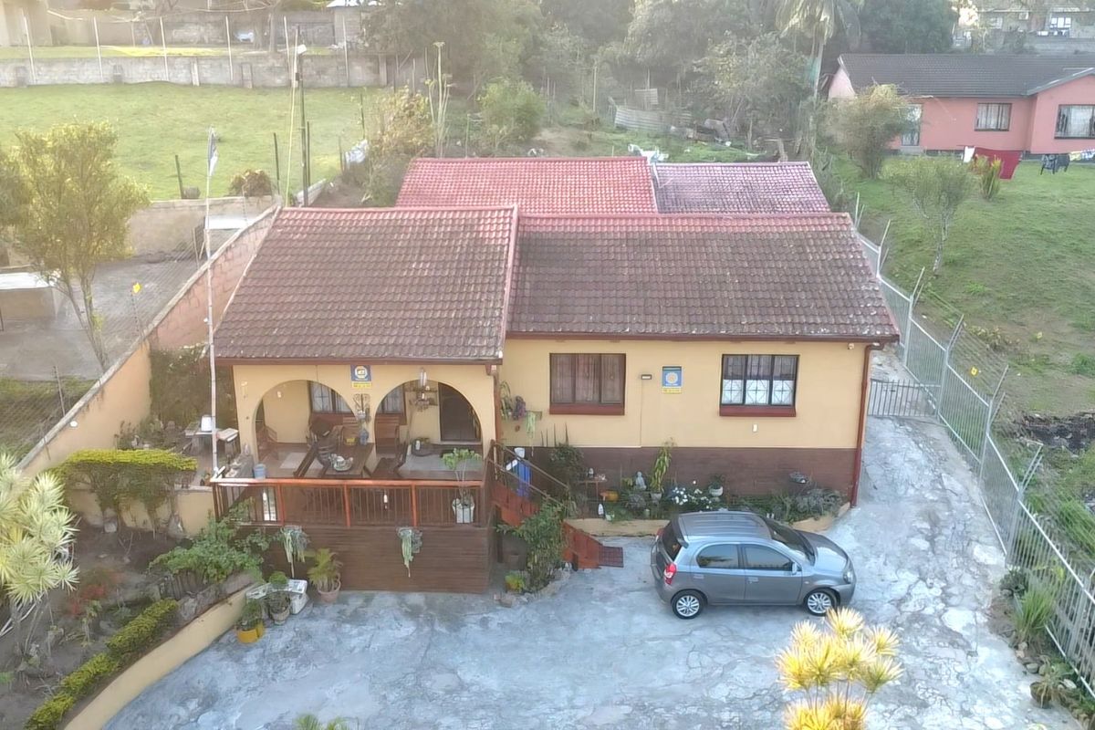 Aerial view of a residential property featuring a tiled roof, covered patio area, and a concrete driveway with perimeter fencing.
