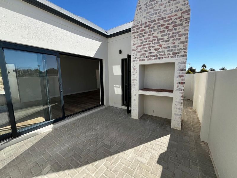 A clean, modern paved patio featuring a built-in brick braai and large sliding glass doors providing seamless access to the interior living space.