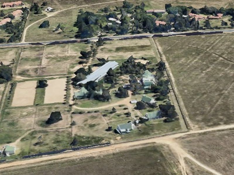 An aerial view of a small holding property featuring multiple structures, fenced paddocks, and established trees within a rural landscape setting.
