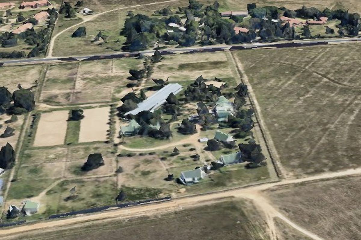 An aerial view of a small holding property featuring multiple structures, fenced paddocks, and established trees within a rural landscape setting.