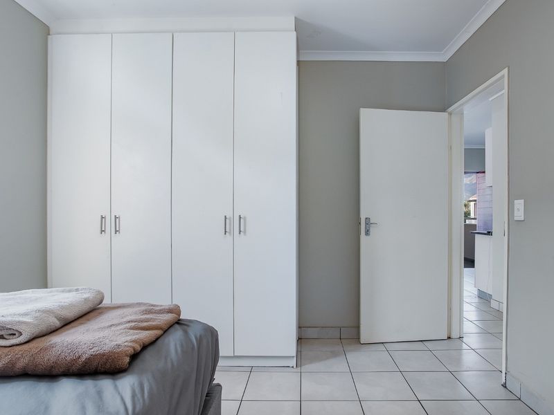 A well-maintained bedroom featuring neutral wall tones, white built-in cupboards, and clean tiled flooring, with direct access to an adjacent room.