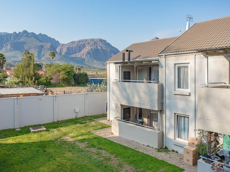 Rear view of the apartment building featuring balconies, a paved patio area, and a private garden with mountain views.