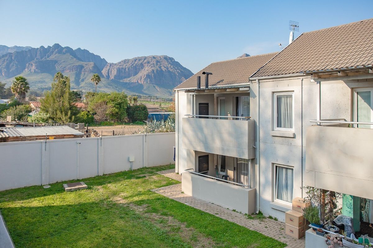 Rear view of the apartment building featuring balconies, a paved patio area, and a private garden with mountain views.