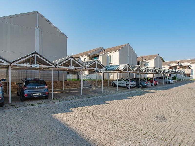Exterior view of the apartment complex featuring a row of covered parking bays and a paved driveway area.