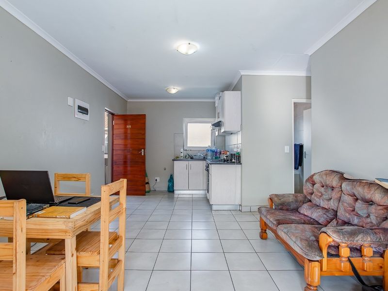 Open-plan living area featuring tiled flooring and a compact kitchen with built-in cabinetry and appliances.