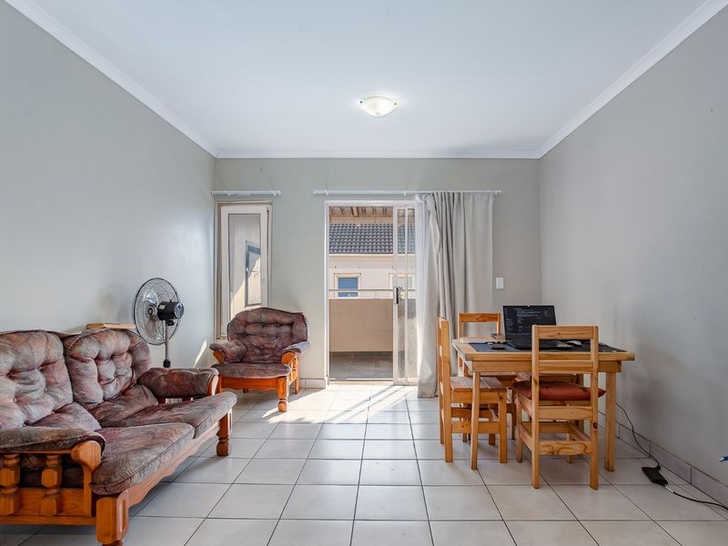 A functional living and dining area featuring neutral wall tones, tiled flooring, and direct access to an outdoor balcony through a sliding glass door.