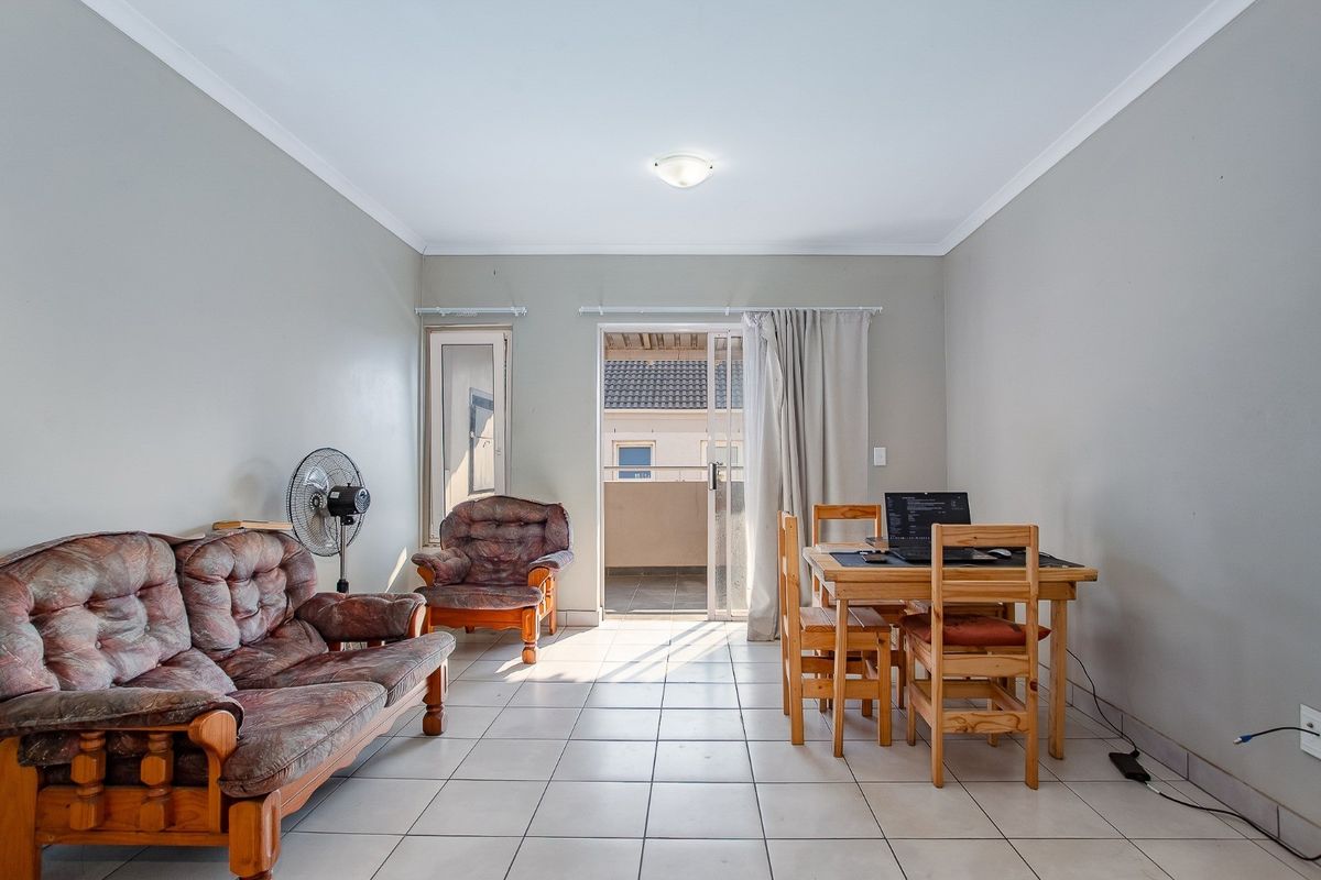 A functional living and dining area featuring neutral wall tones, tiled flooring, and direct access to an outdoor balcony through a sliding glass door.