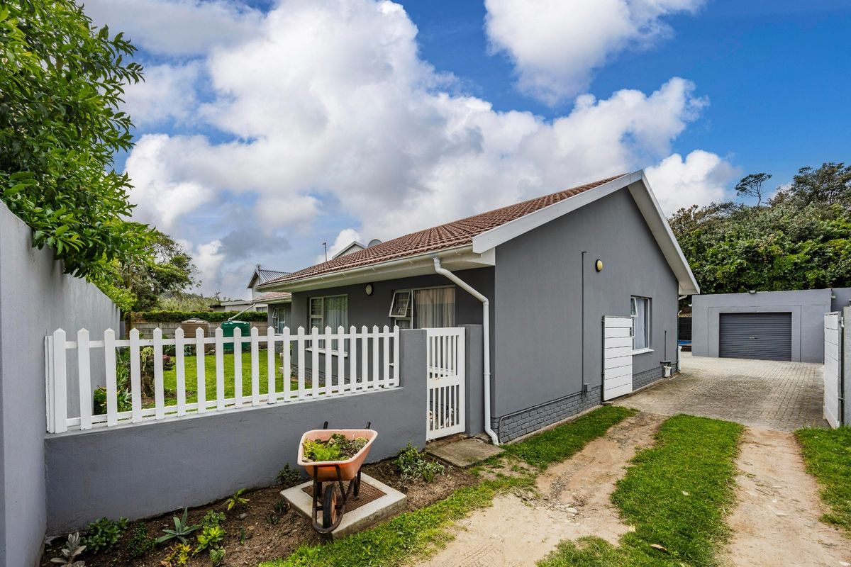 Rear view of the property featuring a tiled roof, paved driveway, detached garage, and a white picket fence enclosing a garden area.