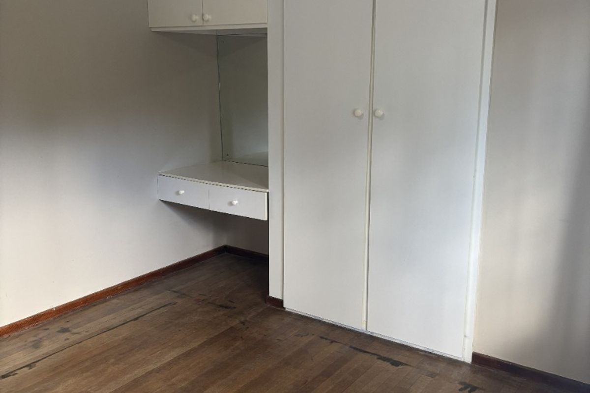 A vacant bedroom featuring original timber flooring, built-in cupboards, and a integrated vanity unit with overhead storage.