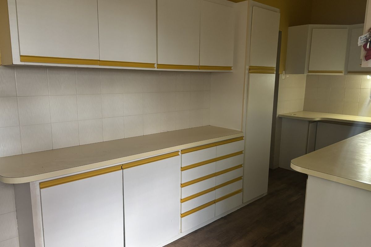 A functional kitchen space featuring white built-in cabinetry with yellow accents, laminate countertops, and tiled backsplash, currently vacant and ready for updates.