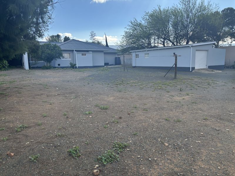 Spacious rear yard area featuring a detached garage and main house structure with metal roofing and neutral exterior paint.
