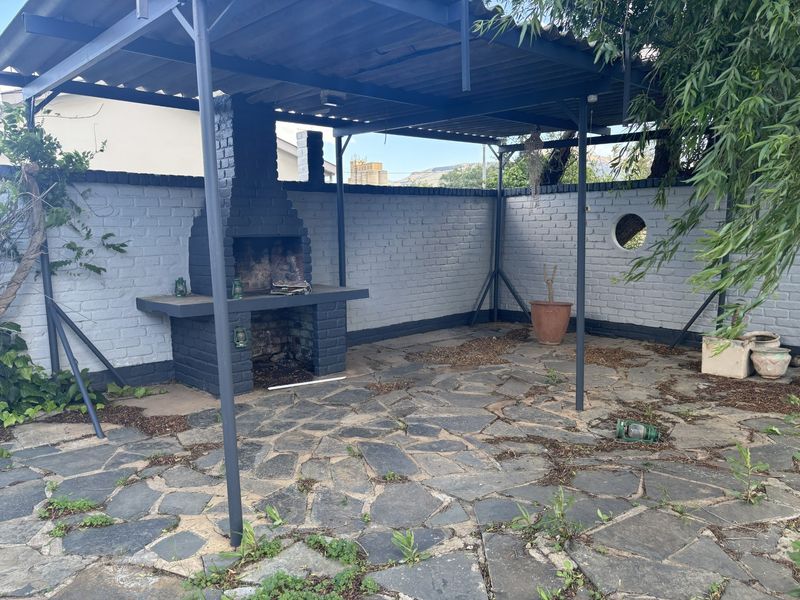 Covered outdoor patio area featuring a built-in brick braai and stone paved flooring, enclosed by a painted brick boundary wall.