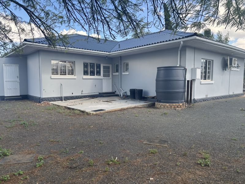 Rear view of the house featuring a concrete patio, water storage tank, and security features on windows and doors.