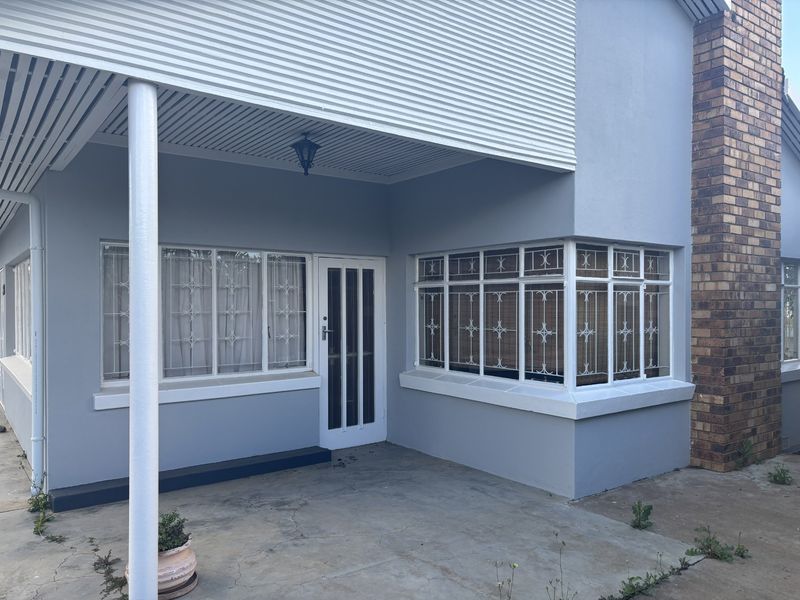 Front exterior view of the house featuring a covered patio area, security-barred windows, and a prominent brick chimney stack.