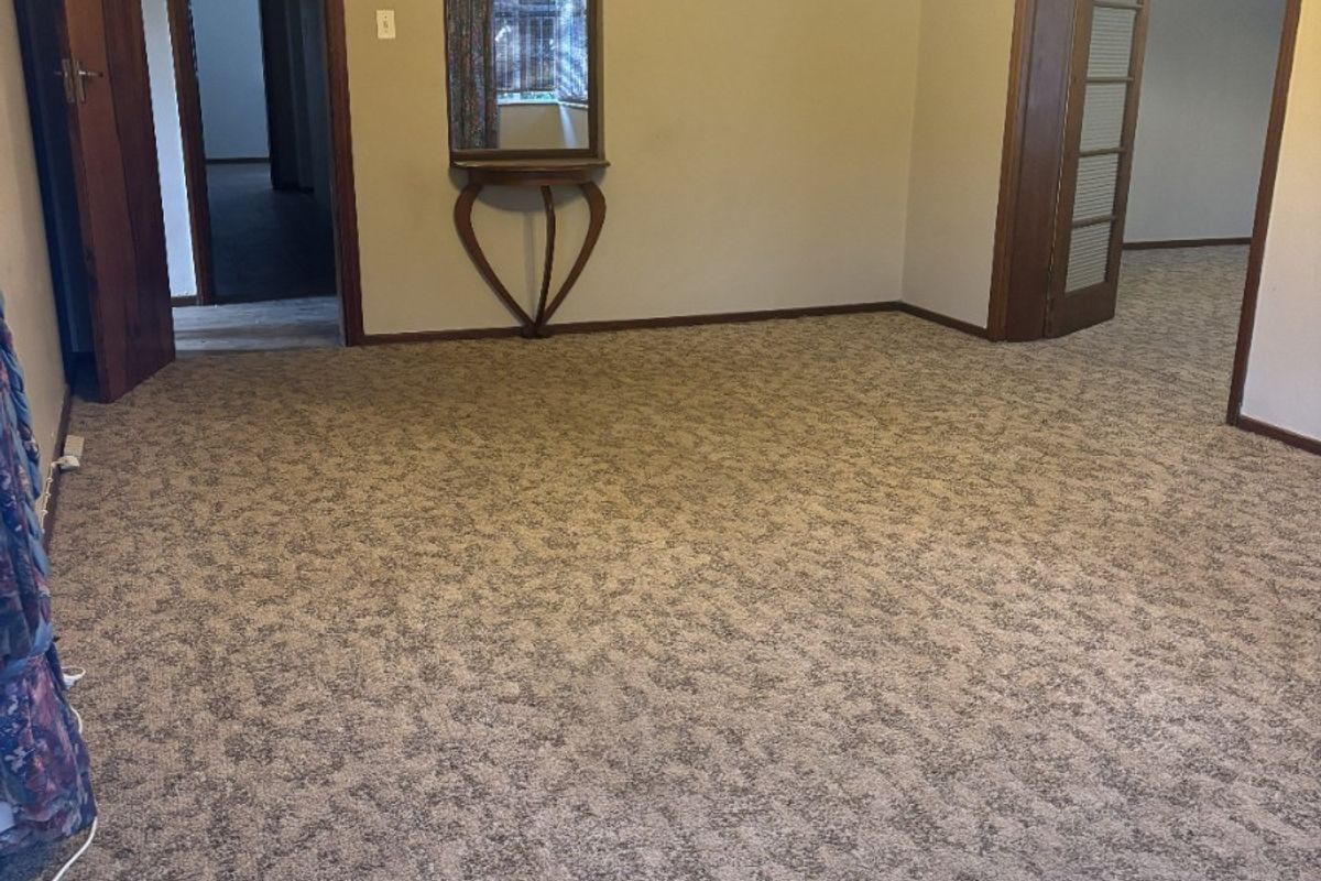 A spacious, empty living room featuring neutral walls, carpet flooring, and traditional timber door frames, offering a blank canvas for renovation.