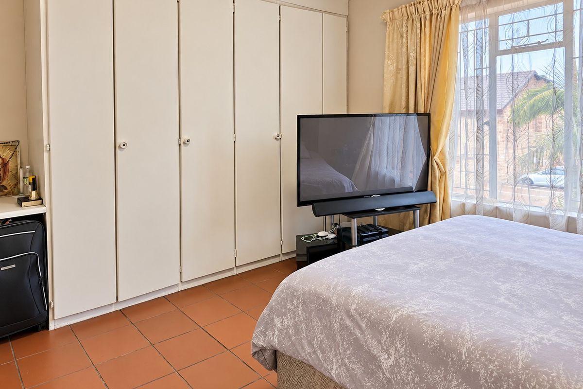 A bedroom featuring built-in cupboards, tiled flooring, and a window with security bars, offering a functional and well-lit living space.