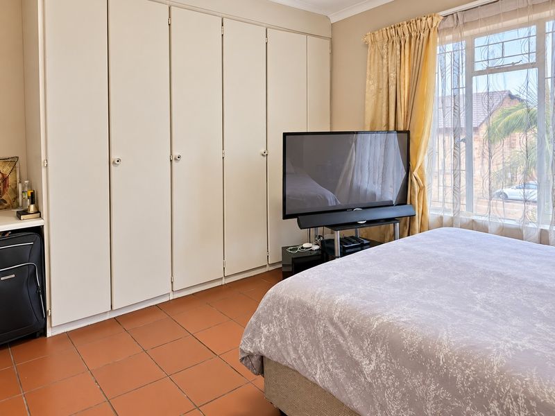 A bedroom featuring built-in cupboards, tiled flooring, and a window with security bars, offering a functional and well-lit living space.