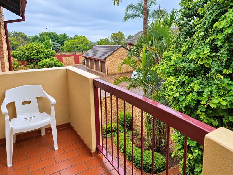 A private balcony featuring tiled flooring and a metal balustrade, overlooking the complex grounds and garden area.