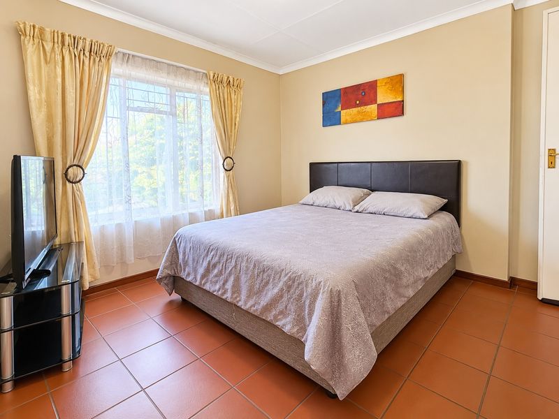 A well-lit bedroom featuring terracotta-style floor tiles, neutral wall finishes, and a window fitted with security bars.