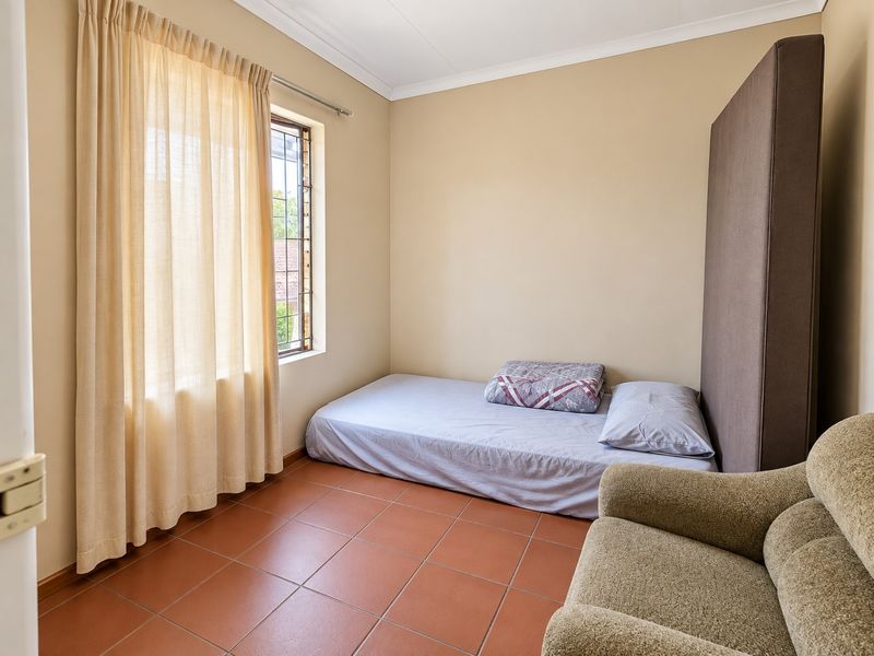 A functional bedroom featuring tiled flooring, a window with security bars, and neutral wall finishes, offering a simple and practical living space.