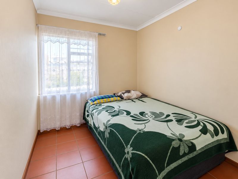 A compact bedroom featuring tiled flooring, neutral wall finishes, and a window with natural light.