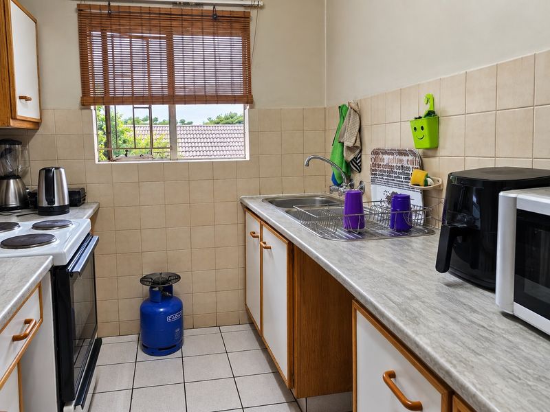 A functional kitchen featuring laminate countertops, tiled backsplash, ceramic flooring, and built-in cabinetry with a freestanding stove.