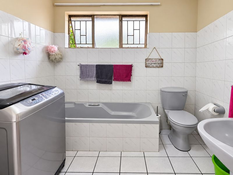 A functional bathroom featuring a built-in bathtub, pedestal basin, and toilet, with tiled finishes and a window with security bars.