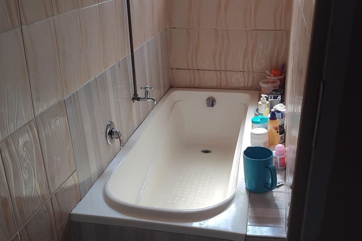 A compact bathroom featuring a built-in bathtub with wall-mounted fixtures and full-height ceramic wall tiling.