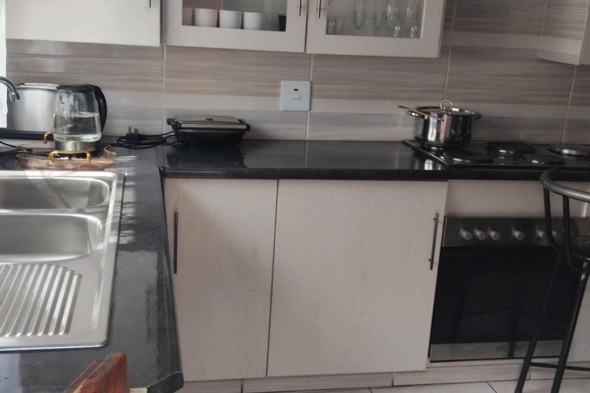 A functional kitchen featuring granite countertops, a double sink, built-in oven, electric hob, and ample upper and lower cabinetry with a tiled backsplash.