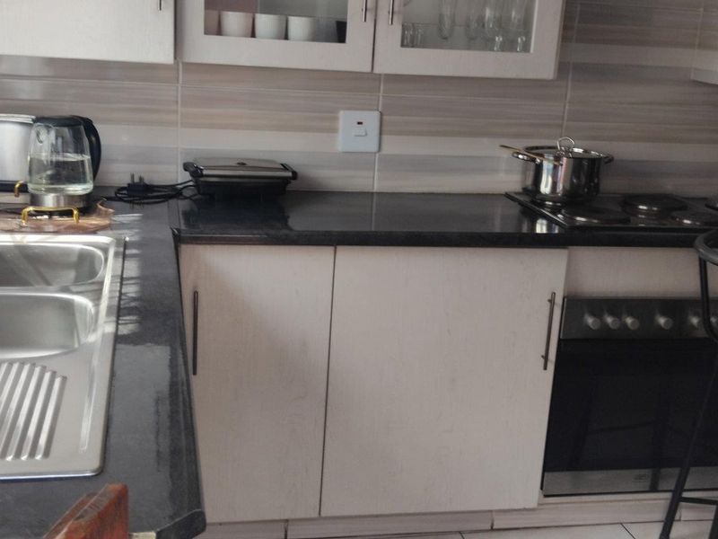 A functional kitchen featuring granite countertops, a double sink, built-in oven, electric hob, and ample upper and lower cabinetry with a tiled backsplash.