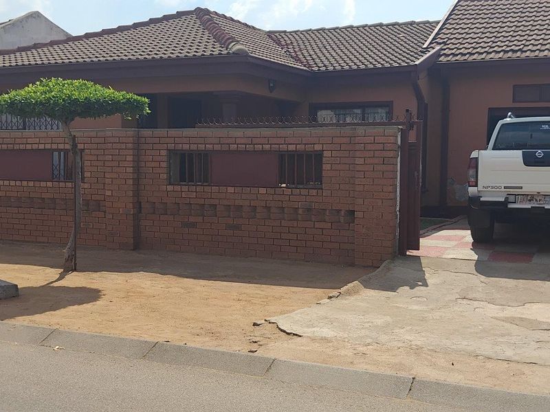 Front elevation of a single-story house featuring a brick boundary wall, tiled roof, and a concrete driveway with gated access.