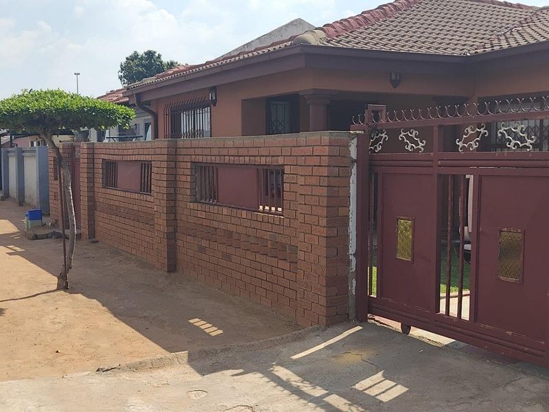 Front exterior view of the property featuring a brick boundary wall, metal sliding gate, and tiled roof structure.