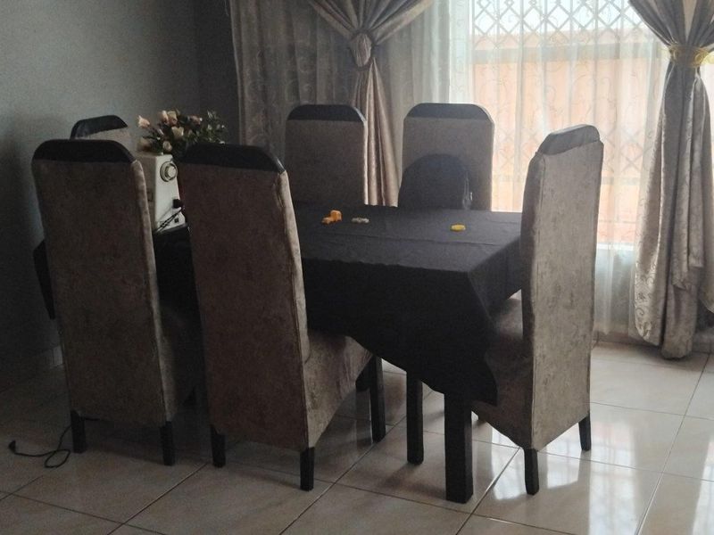 A dining room area featuring tiled flooring and large windows with security gates, providing a functional space for family meals.