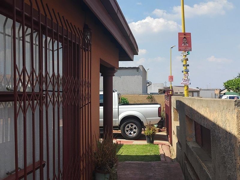 Front exterior view of the property featuring a boundary wall, metal driveway gate, and security bars on the windows.