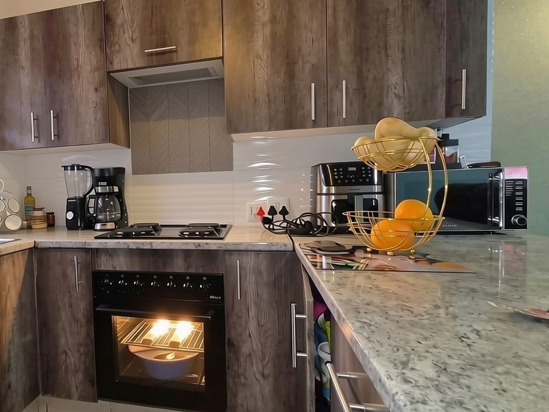Modern kitchen featuring wood-grain cabinetry, stone-look countertops, built-in oven, gas hob, and a tiled backsplash.