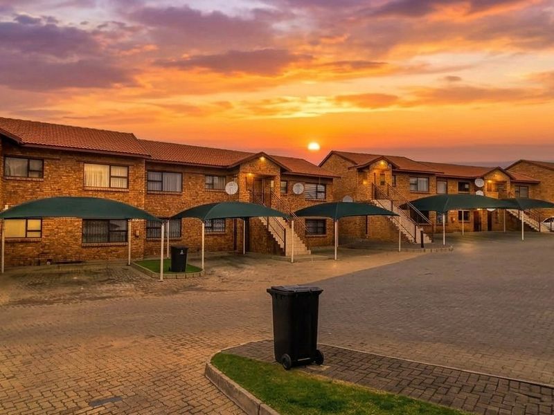 Exterior view of a face brick apartment complex featuring paved parking areas with shade cloth carports and external staircases at sunset.