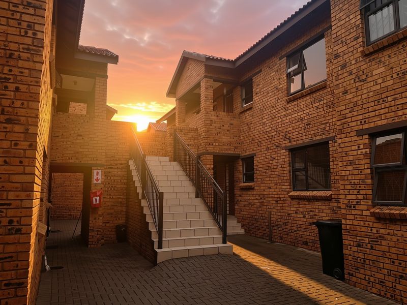 A well-maintained apartment complex courtyard featuring face brick architecture, a central tiled staircase with metal railings, and paved outdoor common areas at sunset.