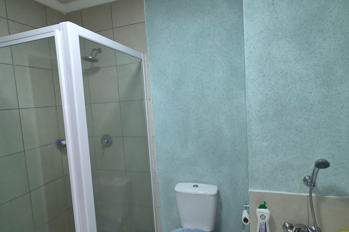 A functional bathroom featuring a glass shower enclosure, a standard toilet, and tiled wall finishes.