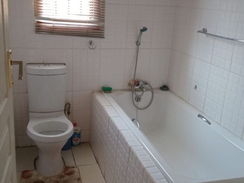 A functional bathroom featuring a built-in bathtub, toilet, and tiled finishes, offering a blank canvas for modernization and cosmetic updates.