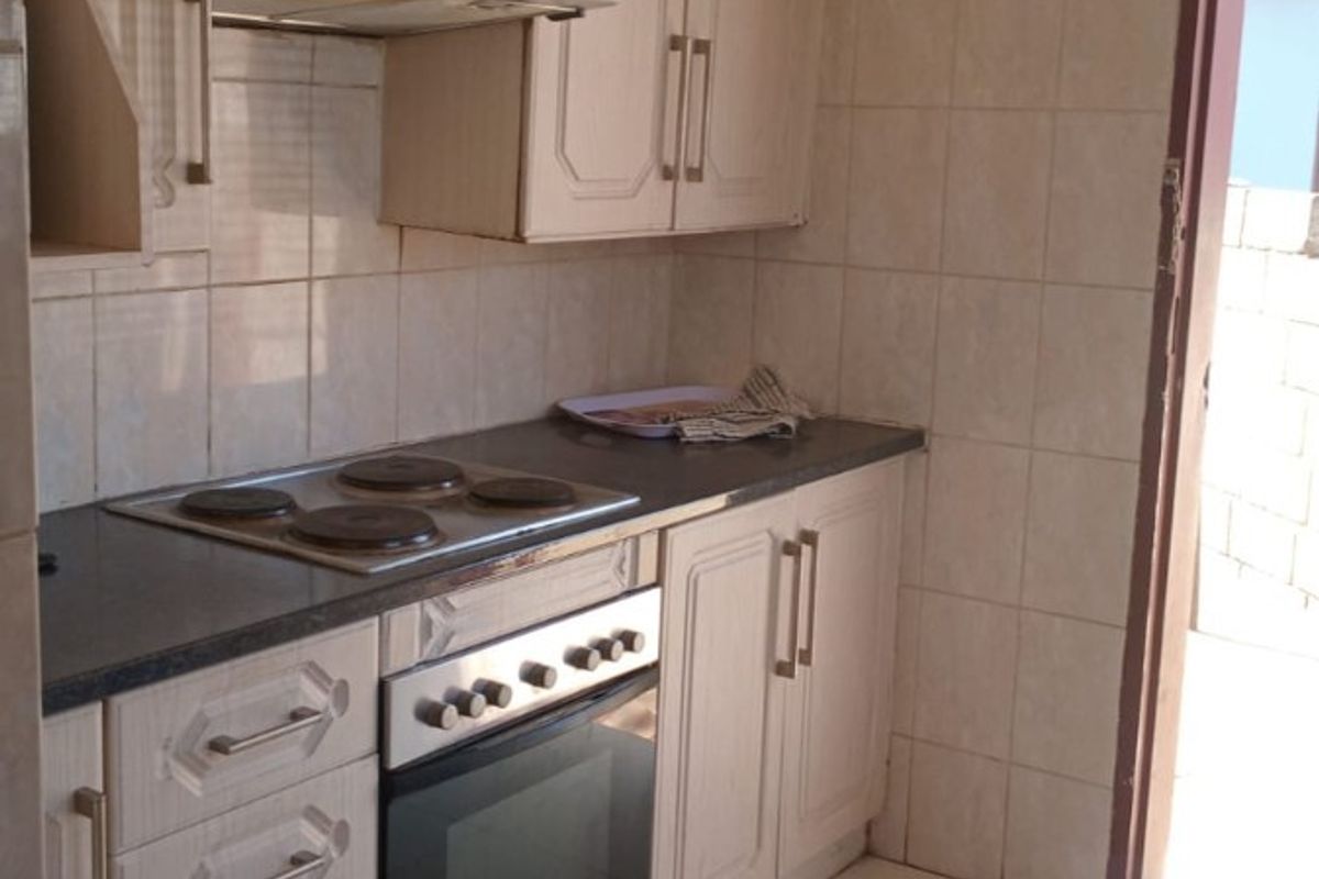 A functional kitchen featuring built-in cabinetry, an electric hob, an oven, and an extractor fan, with tiled walls and flooring throughout.