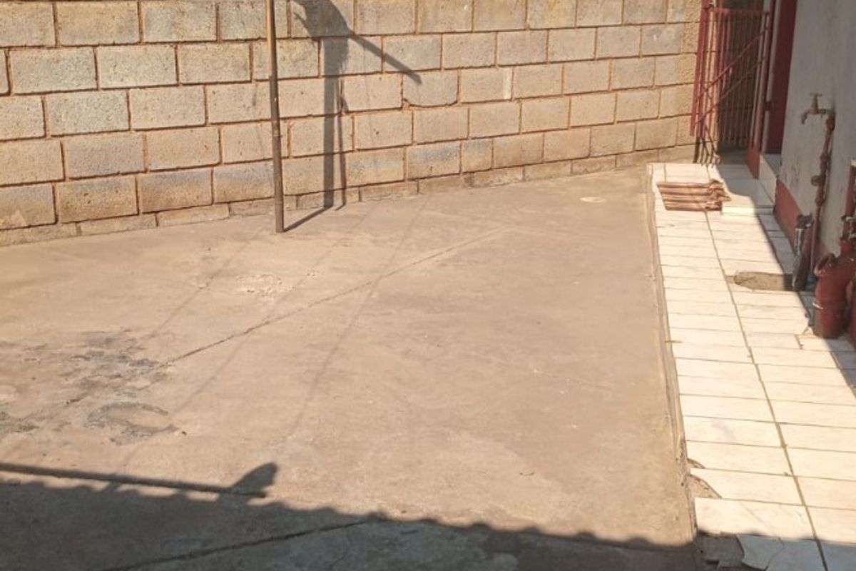 Rear exterior area featuring a concrete boundary wall, tiled walkway, and outdoor water tap, showing signs of wear and damaged paving.